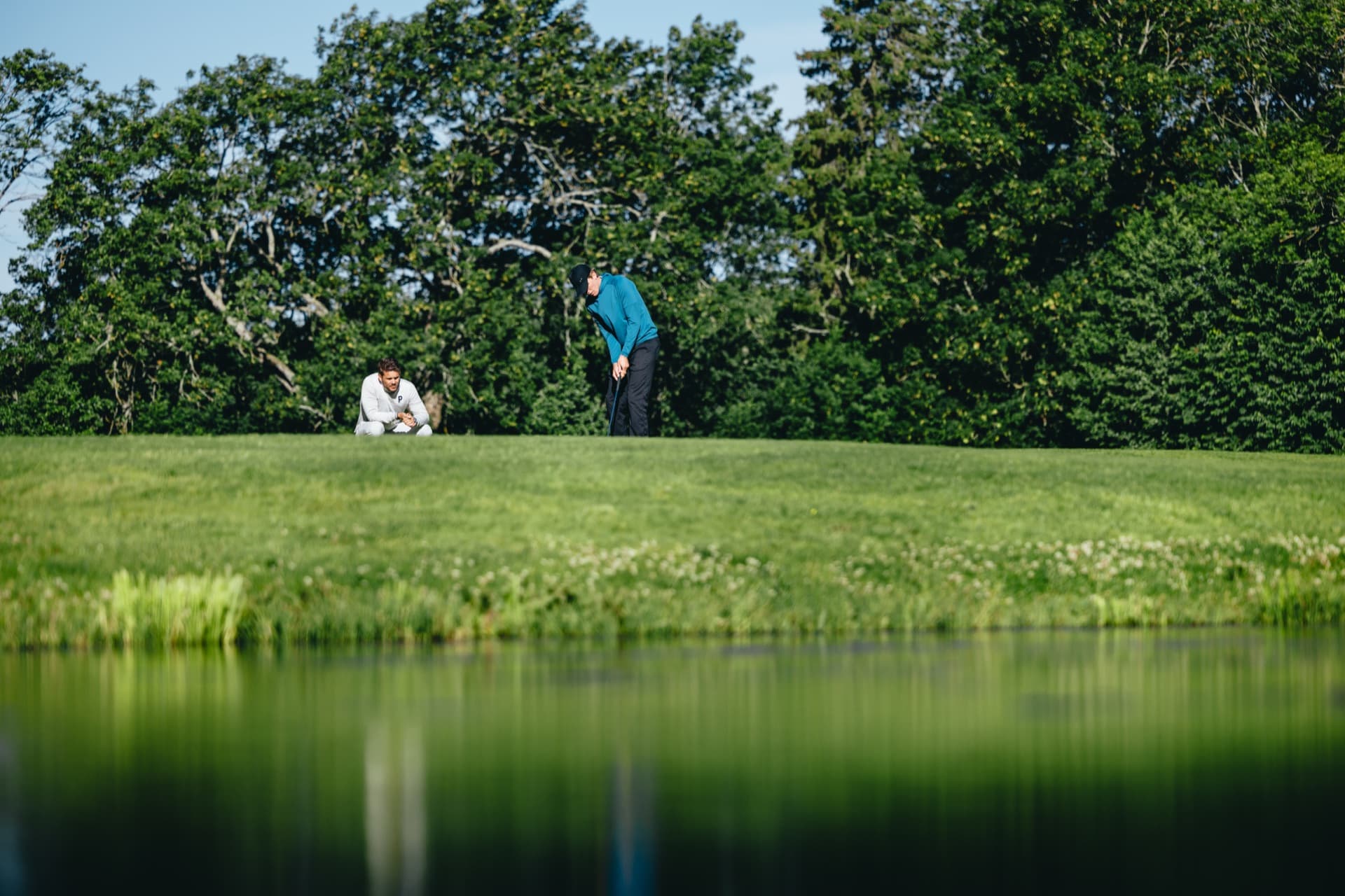 To spillere på putting-grønn med vann-refleksjon i forgrunnen